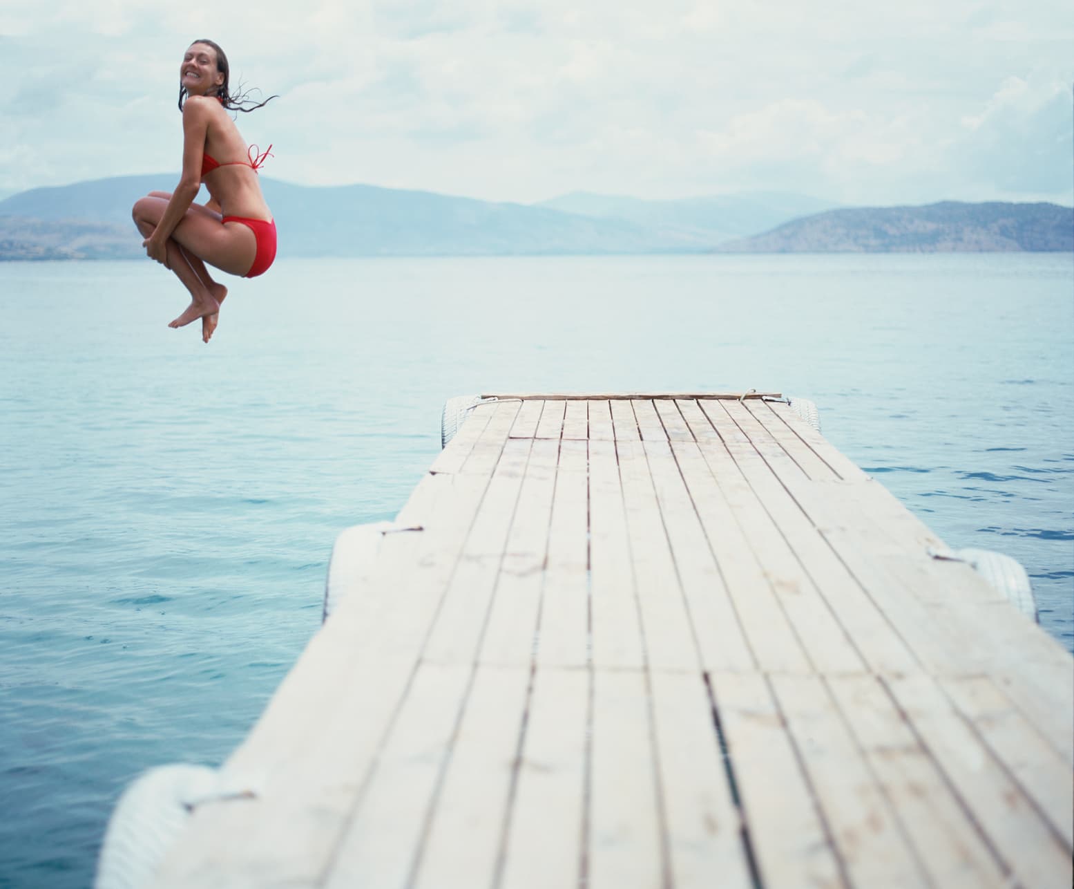Woman jumping off a dock into the ocean